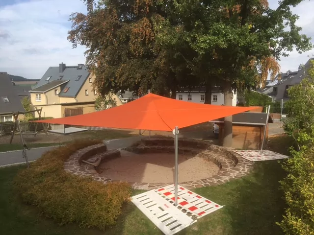 Rotes Sonnensegel mit 4 Masten über einem steinernen Sitzkreis