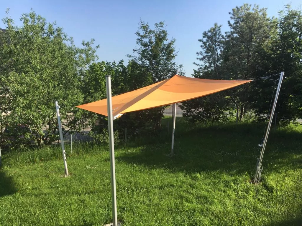 Oranges Sonnensegel mit vier Masten über einer Wiese