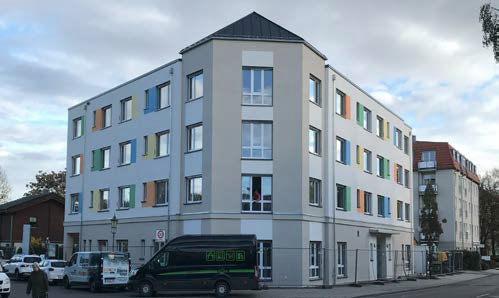 Mehrstöckiges Haus, von vorn, weiße Fassade, gelbe Markisen